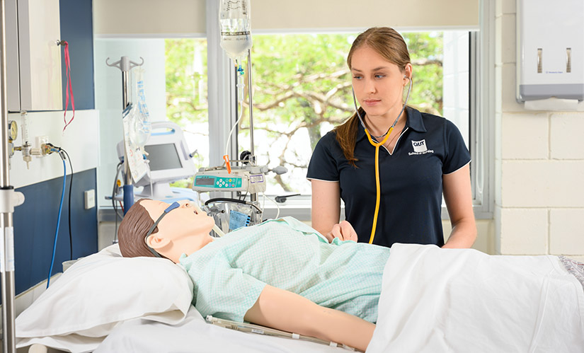 Sarah Evans, Indigenous scholarship recipient, wearing a nurses' uniform stands in front of a hospital bed and equipment.