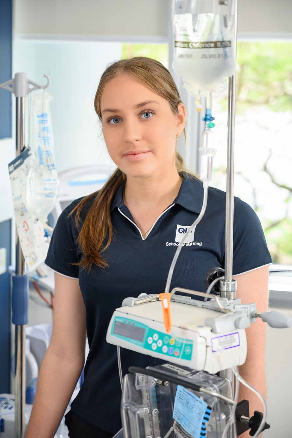 Sarah Evans, Indigenous scholarship recipient, wearing a nurses' uniform stands in front of a hospital bed and equipment.