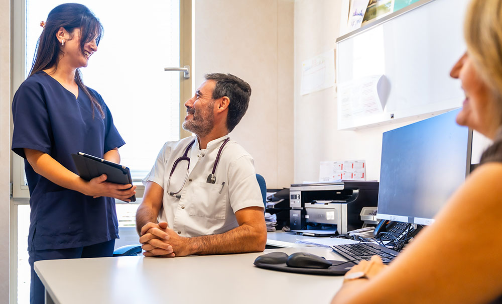 A female nurse in dark blue scrubs checks patient information with her supervisor.