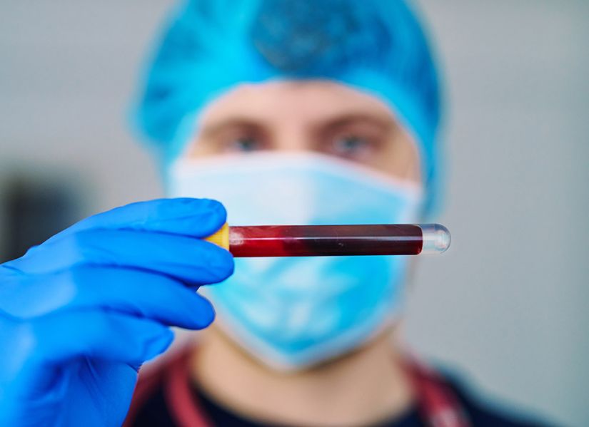 A nurse in full protective clothing holds up a vial of blood.