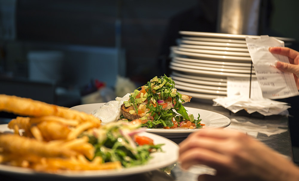 A plate piled high with fresh salad and a plate of chips are placed on a service counter for wait staff to collect and deliver.