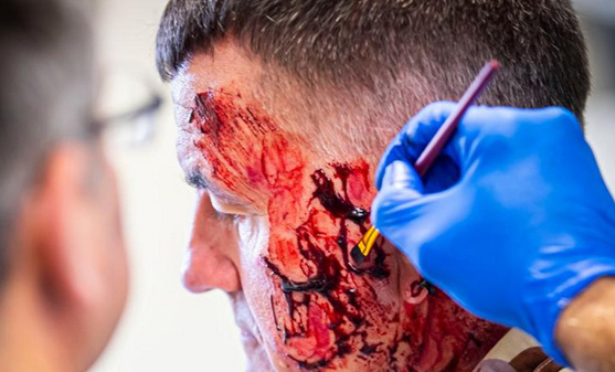 A patient for the simulated scenario has fake blood applied to their cheek to look like a wound.