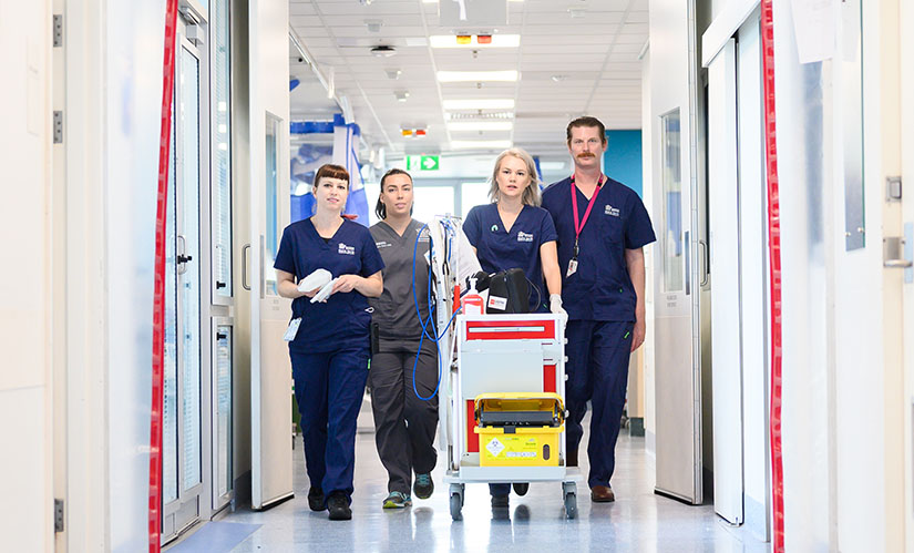 A group of nurses in scrubs walk down a hospital hallway.