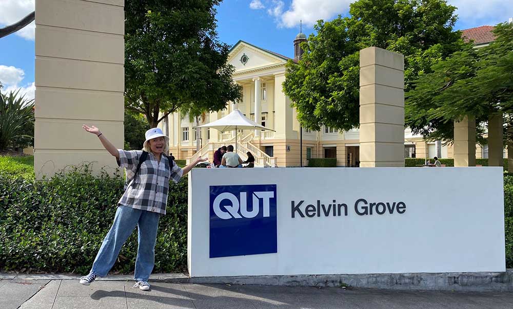A laughing student stands next to a Kelvin Grove campus sign.