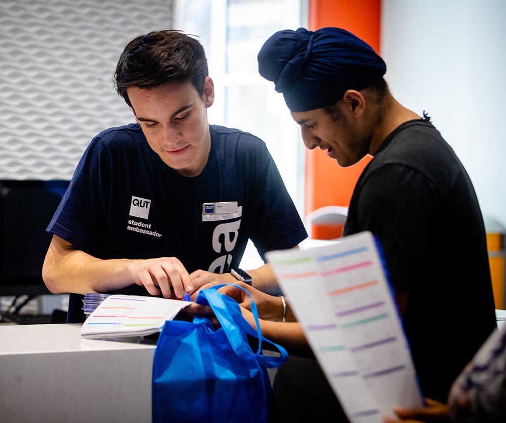 A QUT student in a uniform and hat helps direct a visitor in a Sikh turban.