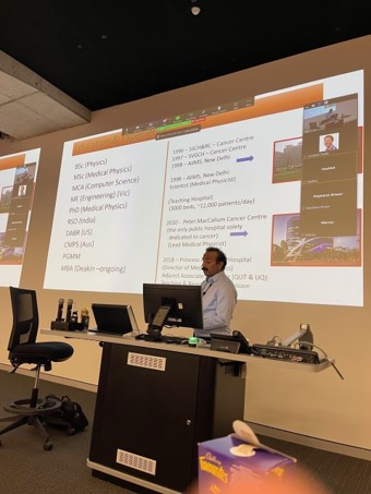 An expert in biomedical science stands at a platform in a lecture theatre delivering a talk to students.