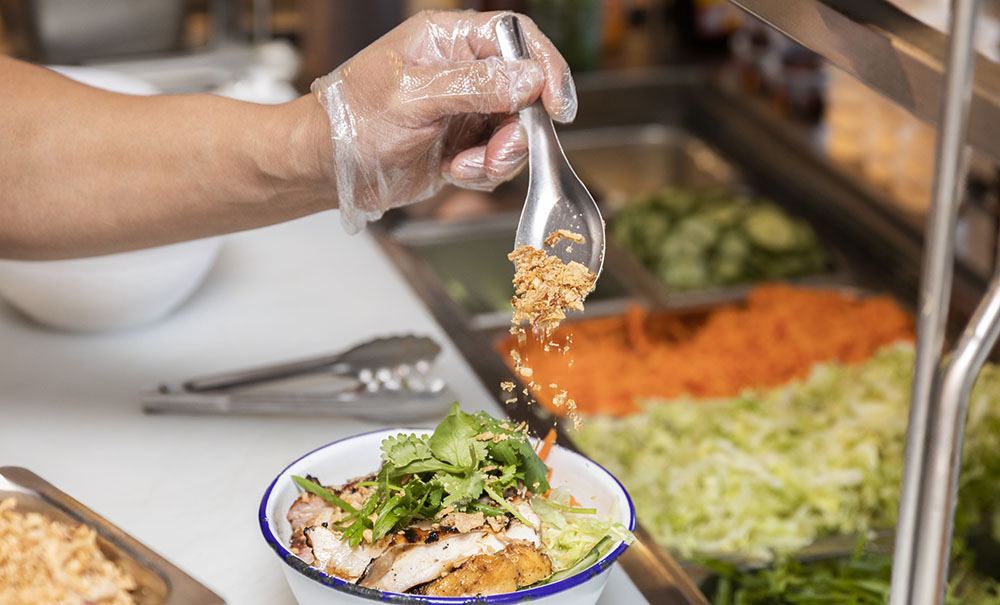 The gloved hand of a chef sprinkles crushed peanuts on a Thai salad.