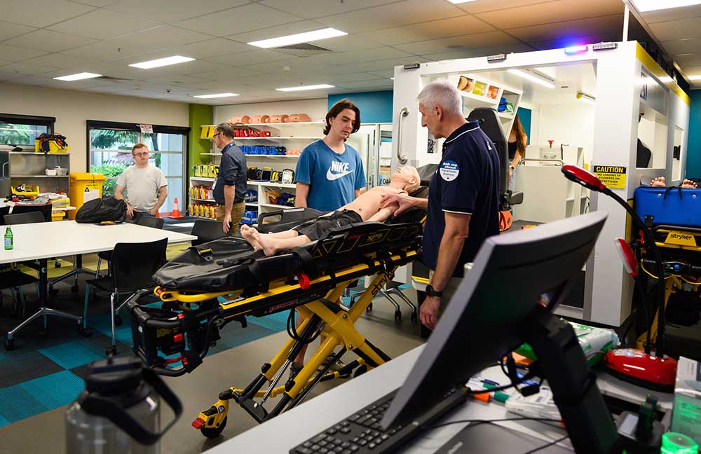 A student standing next to a life-sized ambulance rig talks to an academic.