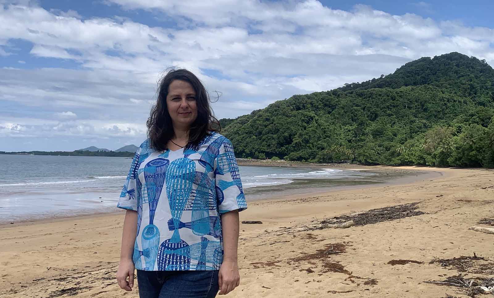 A woman in a clinical uniform stands on a remote beach.