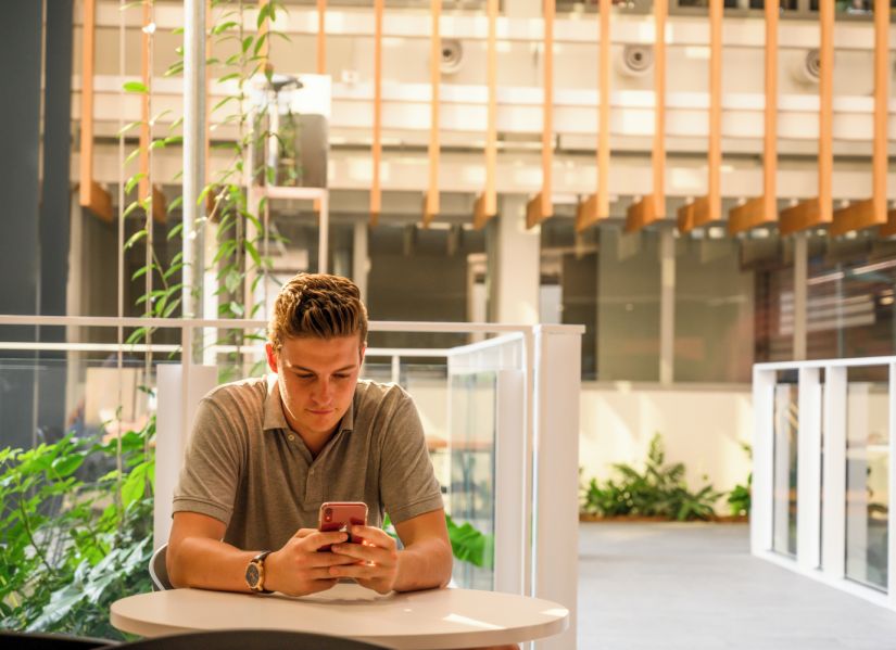 Male student at table, looking at cell phone