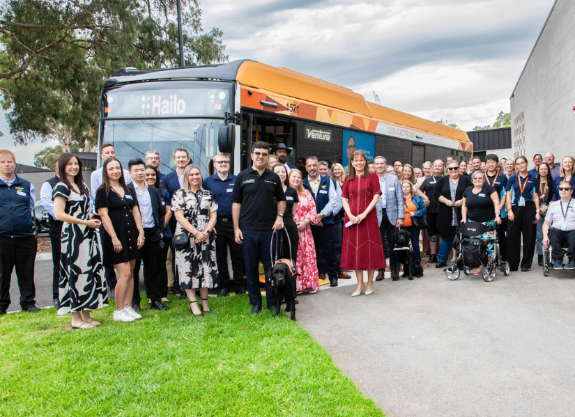 A group of people standing in front of a bus with the bus sign at the front saying Hailo.