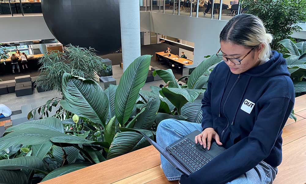 A student sits crossed-legged checking emails on her laptop.