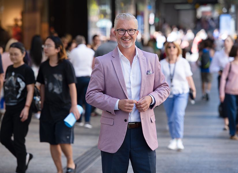 A man standing in the middle of a busy mall, smiling to the camera.