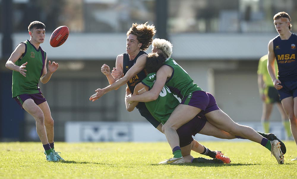 Two young men in a rubgy game tackle another man as he passes the ball.