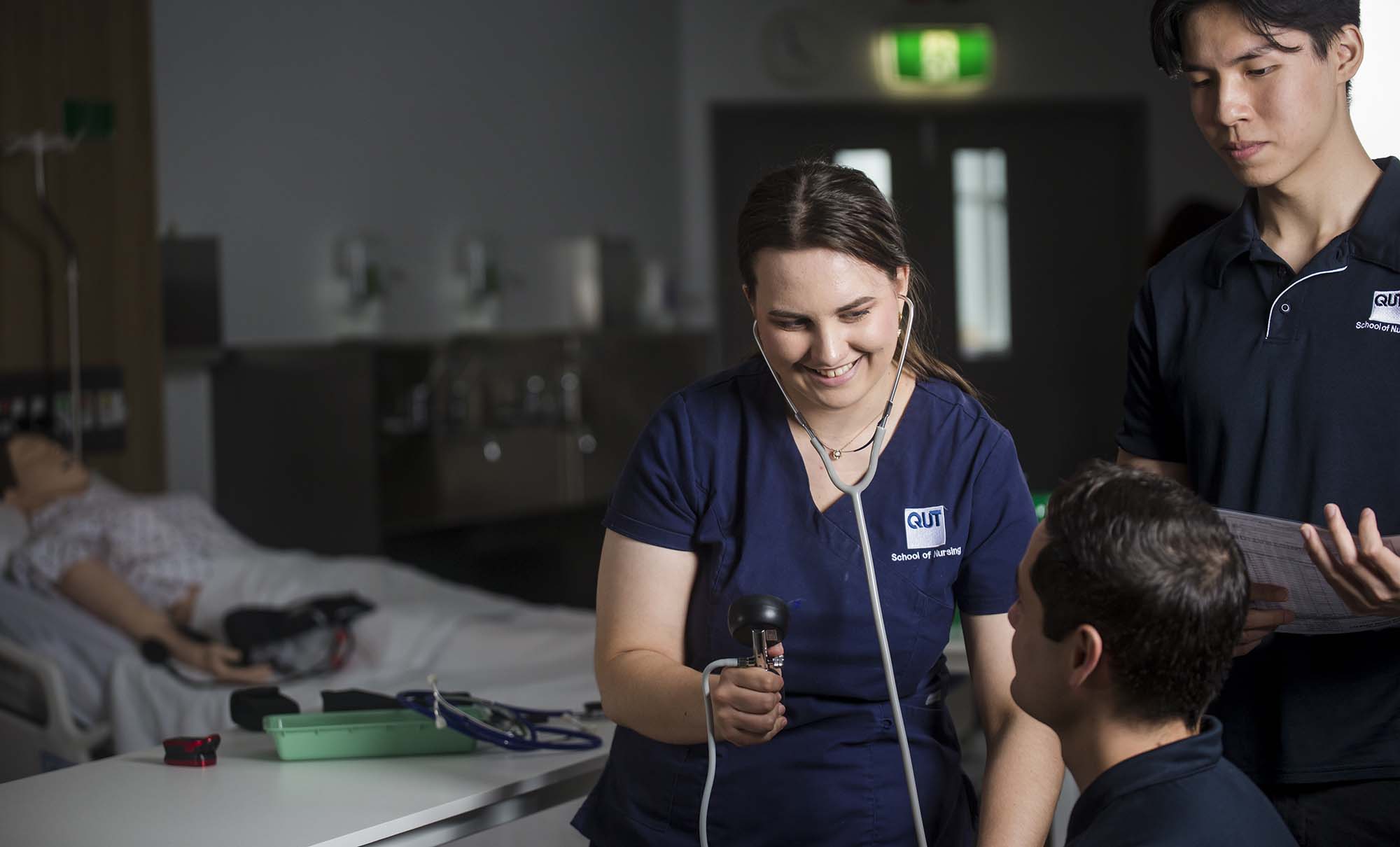 Three nursing students laugh as they practice a technique in a classroom.