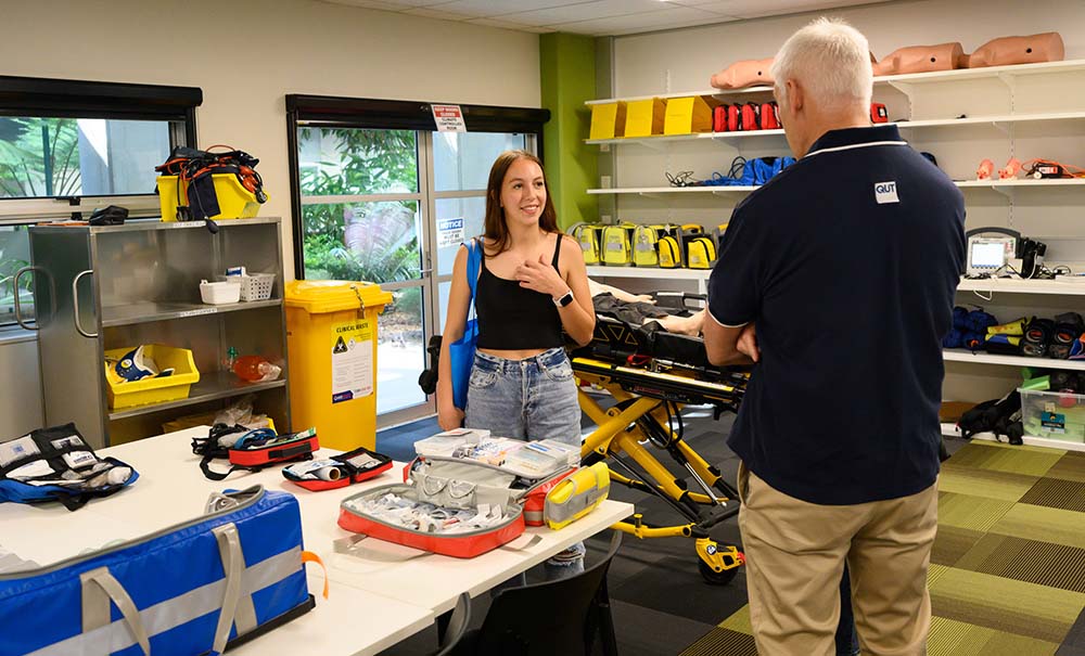 A female student chats with a paramedic science lecturer. Around them are tables set up with practice dummies and equipment and medicines that paramedics use to treat patients.