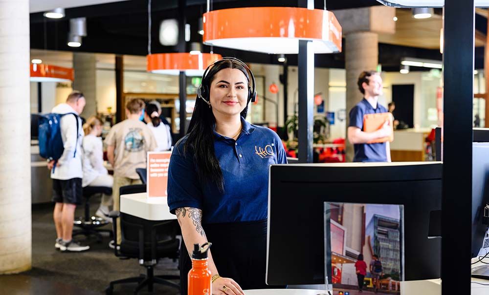 A woman in a HiQ polo shirt stands at a kiosk waiting to help student inquiries.