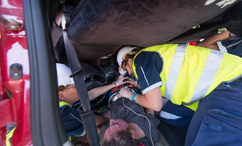 Paramedic science students participate in a training activity treating a pretend patient in an upside down car.