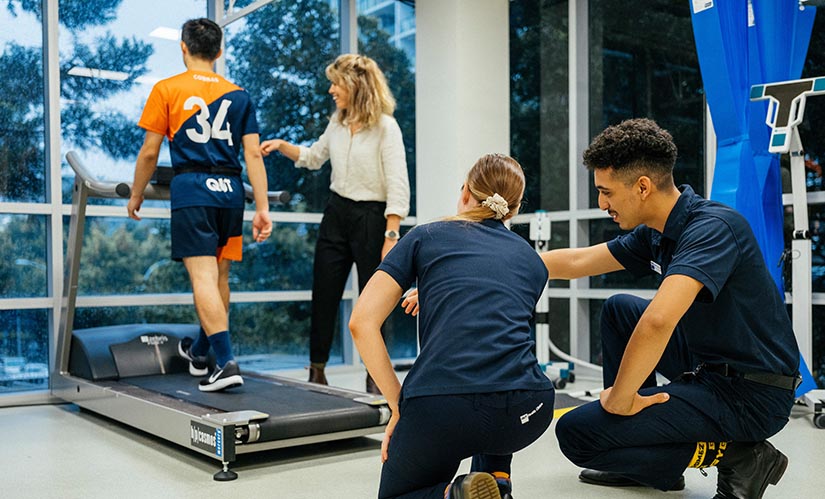 Two podiatry students monitor the gait of a sports player as they walk on a treadmill.