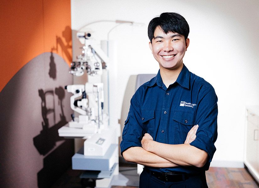 A smiling student stands in an optometry consultation room.