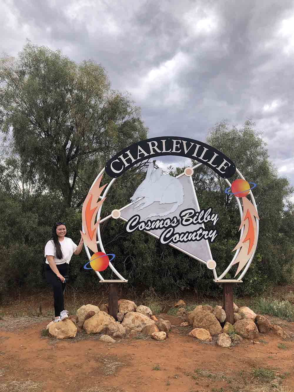 A woman stand in front of a sign reading 'Charleville - cosmos bilby country'.