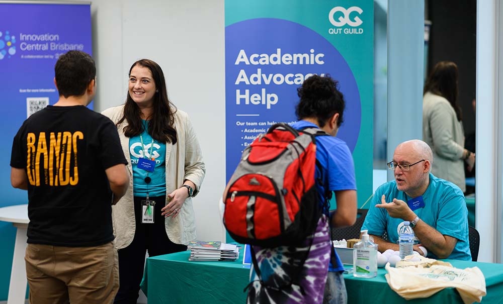A male student talks to a student support officer, while a female student wearing a backpack finds out more about what help is available from a man sitting at the student support table.