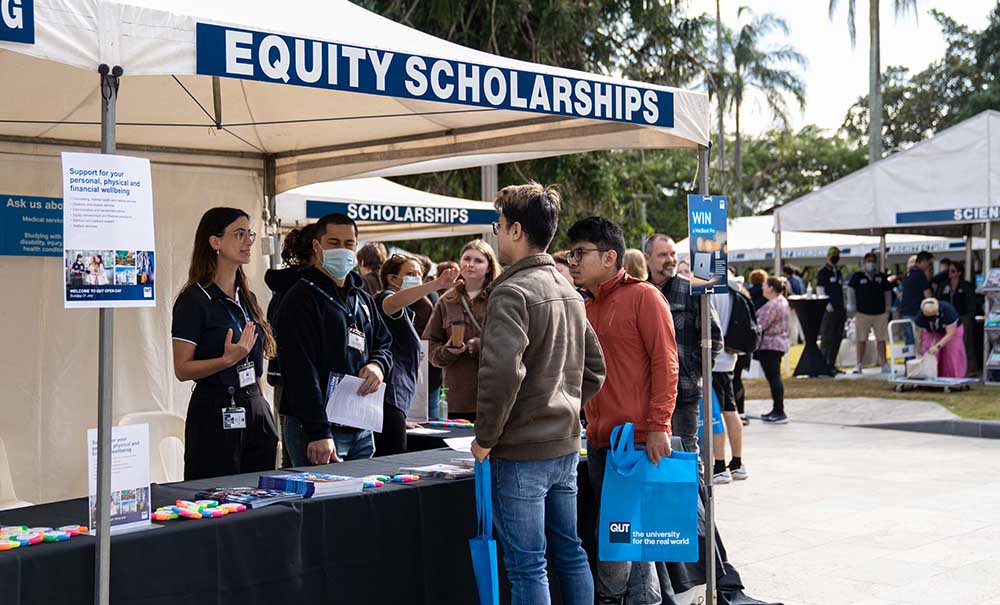 A crowd stands in front of a tent at Open Day chatting with academic staff. The sign on the tent reads Equity scholarships.