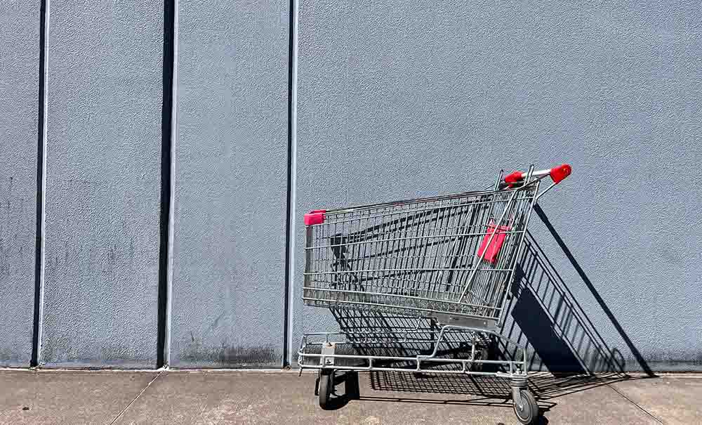 An empty grocery trolley sits in a concrete parking lot.