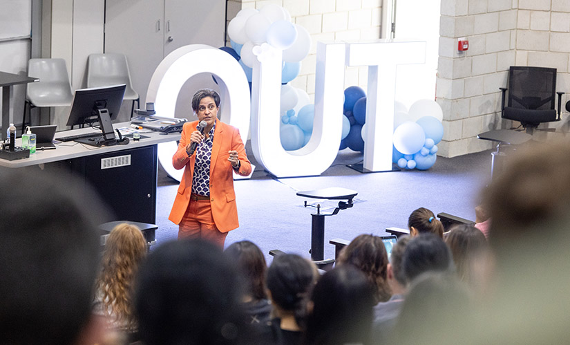 A group of people in a large lecture theatre listen to a female presenter deliver a seminar.