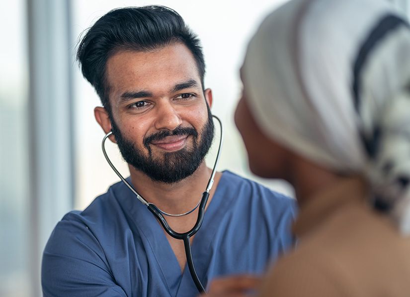 A male nurse smiles as he consults with a female patient wearing a headscarf.