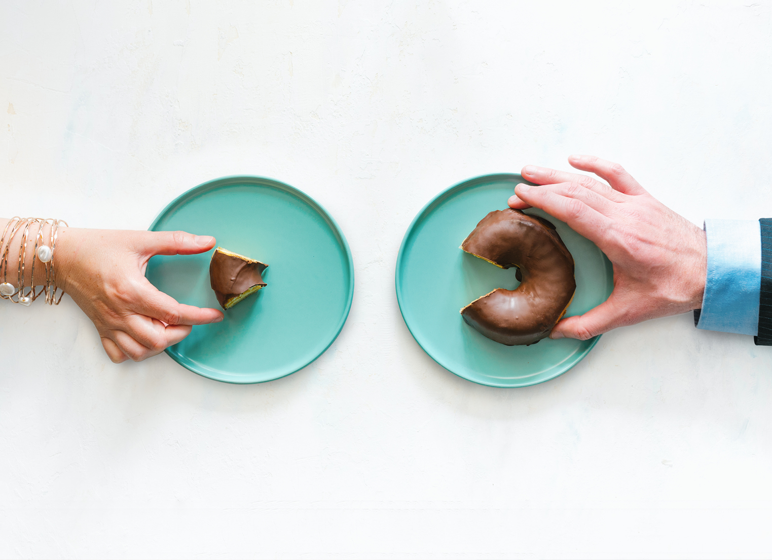Two hands, one with small piece of donut another with large piece