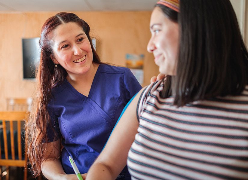 A female healthcare worker in scrubs smiles as she chats to a larger bodied female patient.