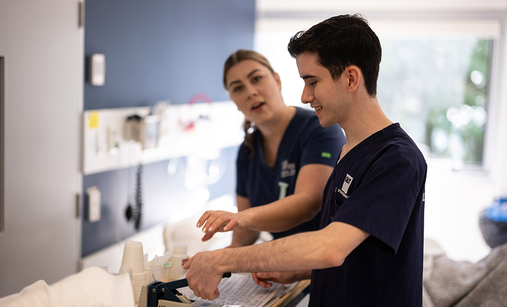 A male and a female nursing student stand at a desk preparing a treatment. They are working together to respond quickly.