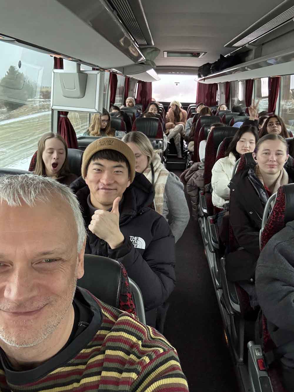 A professor and a group of students on a bus smile at the camera.