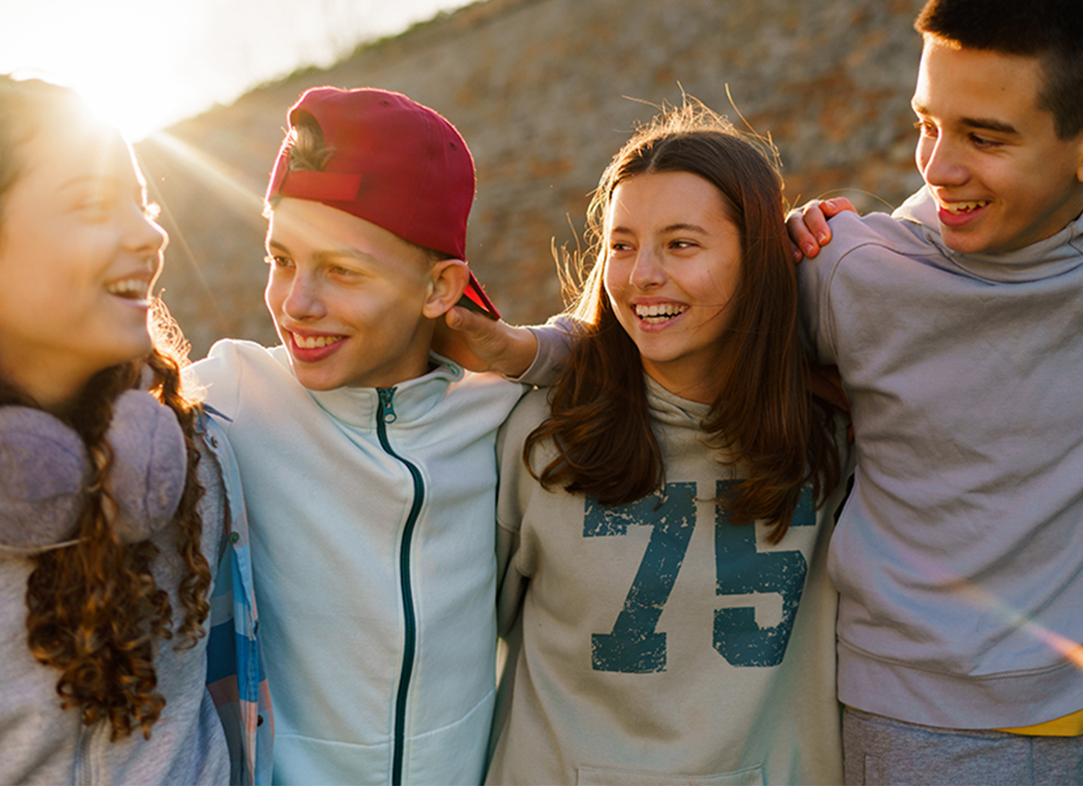 Happy teenage children are standing with their arms around each other outside.