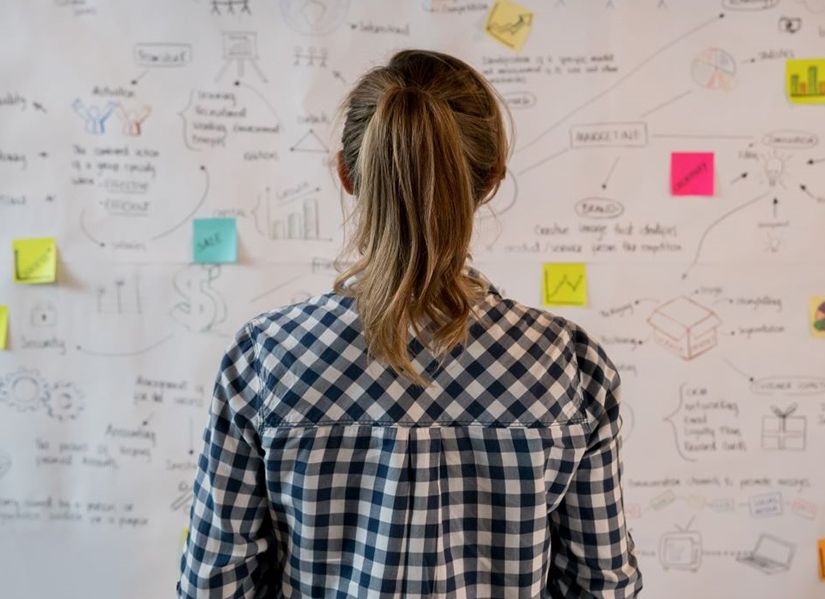 Women with brunette ponytail looking at post-in notes on a wall
