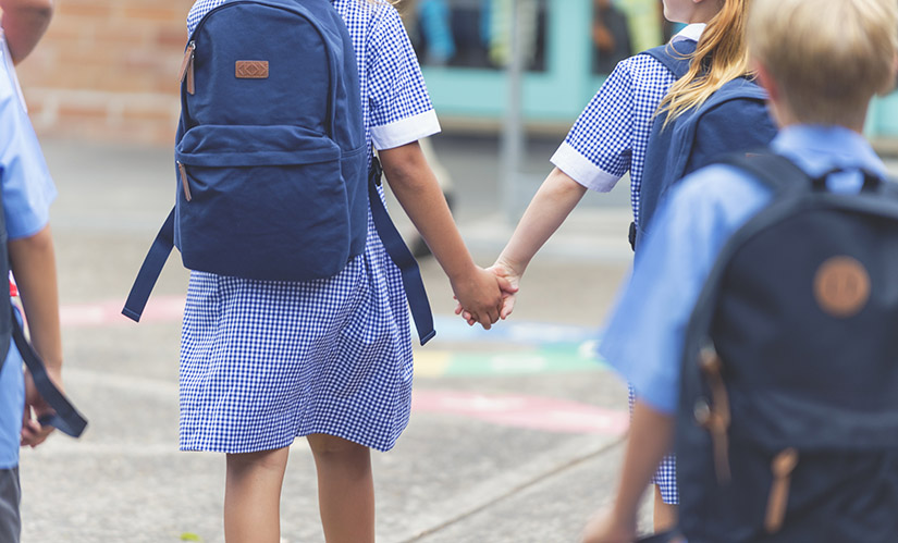 Two girls in uniform holding hands walk towards their classroom.