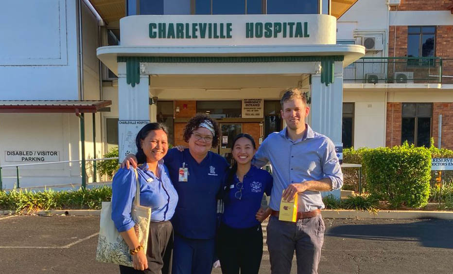 A group of smiling pharmacists stand in front of a hospital entrance.