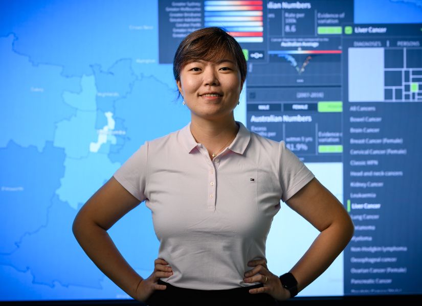 QUT Master of Data Analytics student Sally standing in front of a data wall displaying a map and graphs