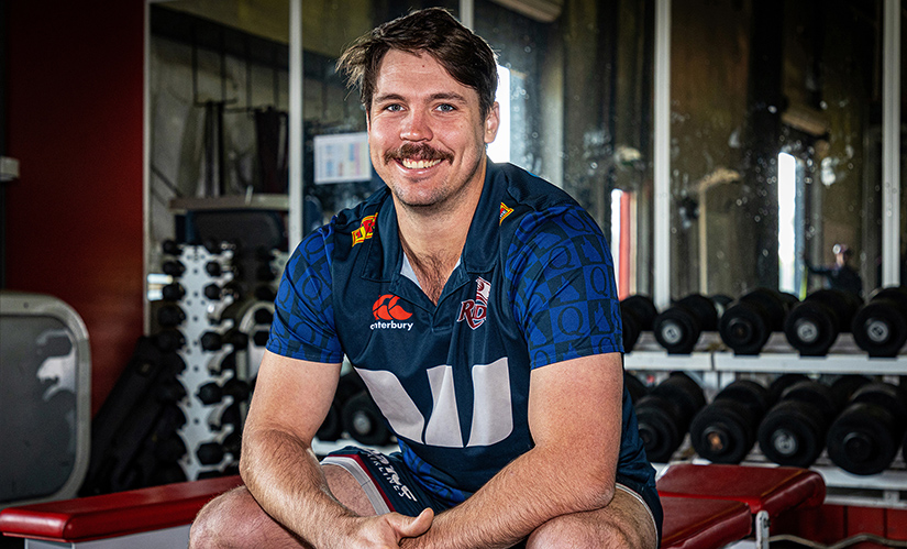 A young male student wearing a polo shirt sits in a weight training facility.
