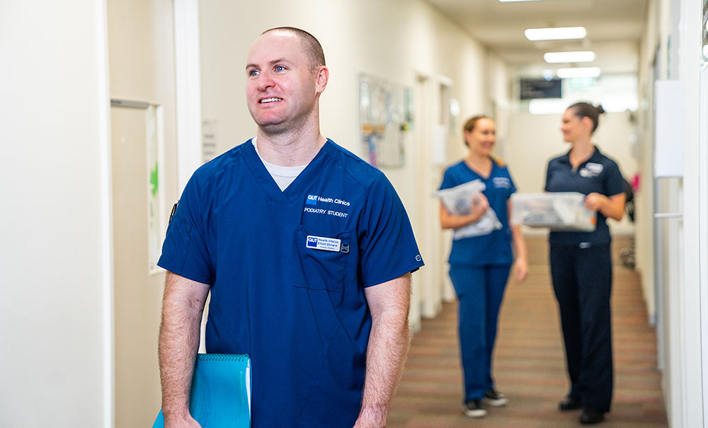 Male student in scrubs walks through the hallway of a clinic.