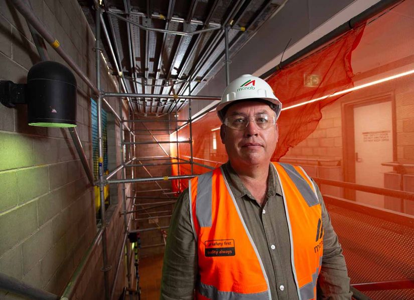 A man wearing a hard hat and high visibility vest stands on a construction site.