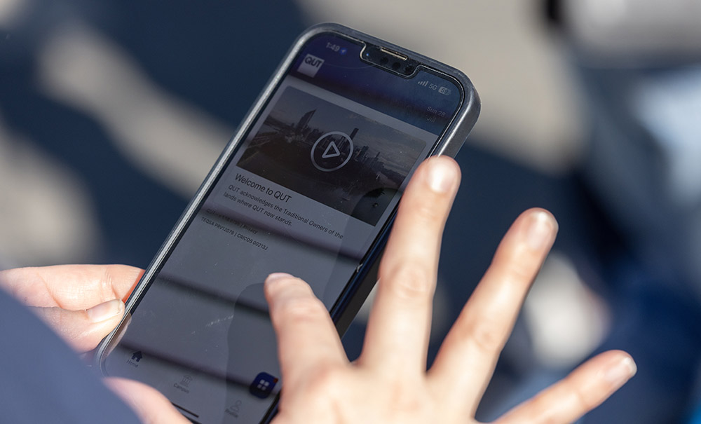 Hands hold a smart phone. On the screen the Welcome message for the QUT app is visible.