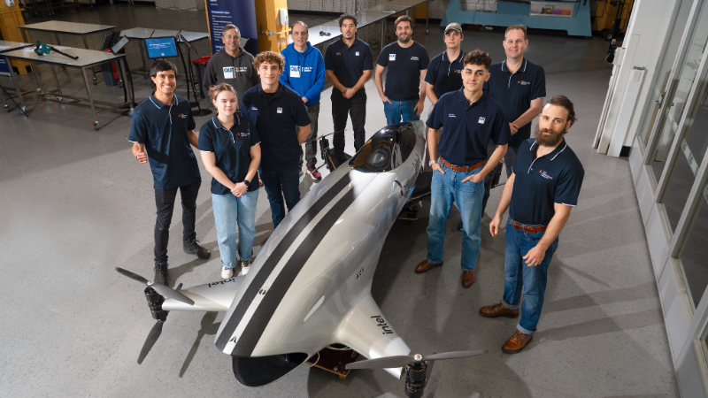 QUT staff and students stand around a flying car.