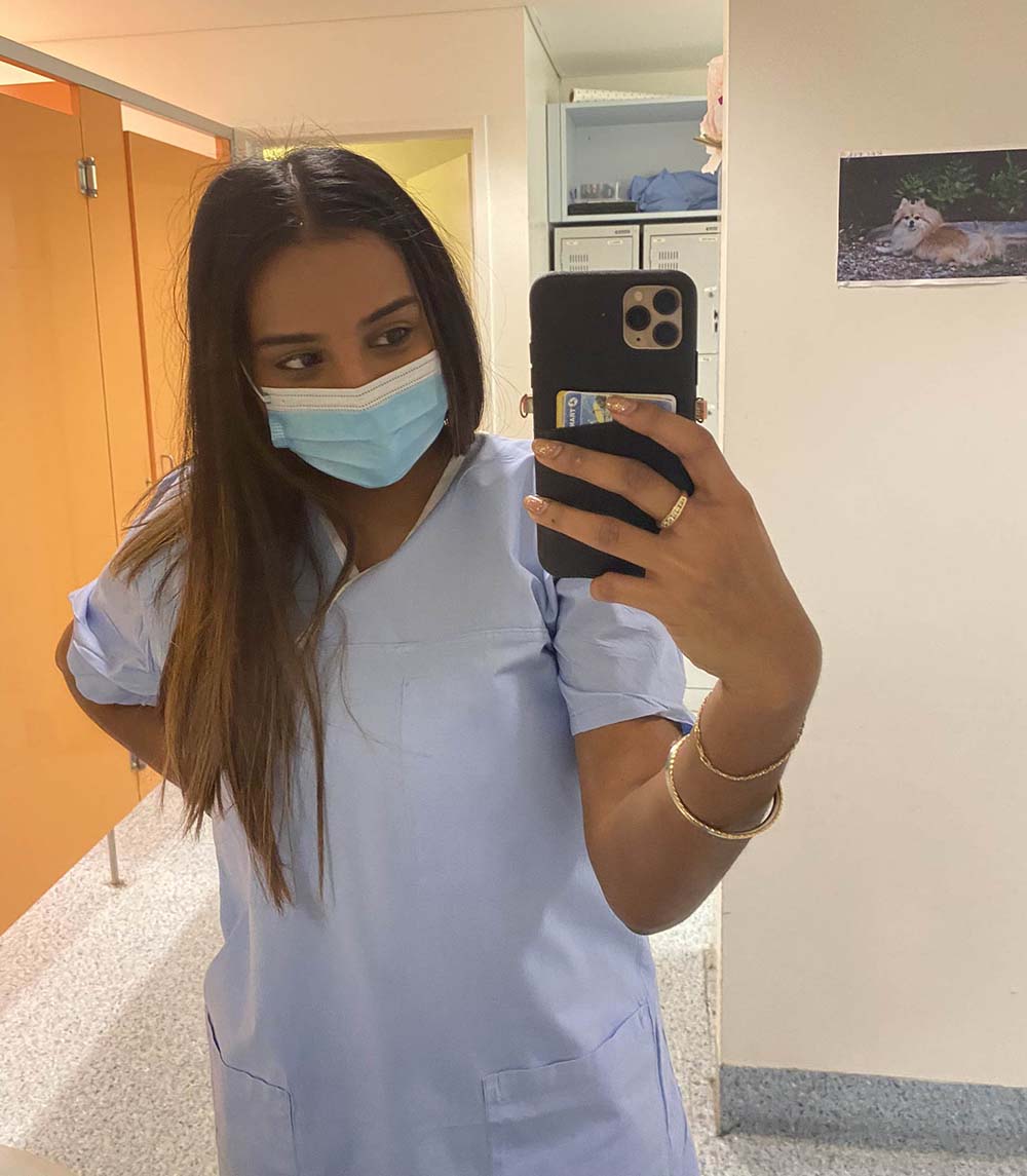 Female student in scrubs stands in a locker room in a hospital.