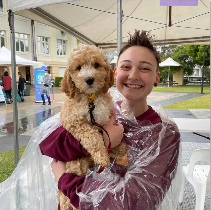 Smiling student stands on campus in a rain jacket while holding the cutest fuffy dog.
