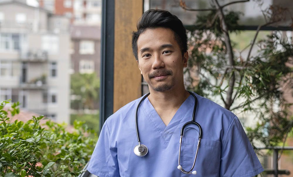 A male nurse practitioner candidate stands on a hospital balcony.