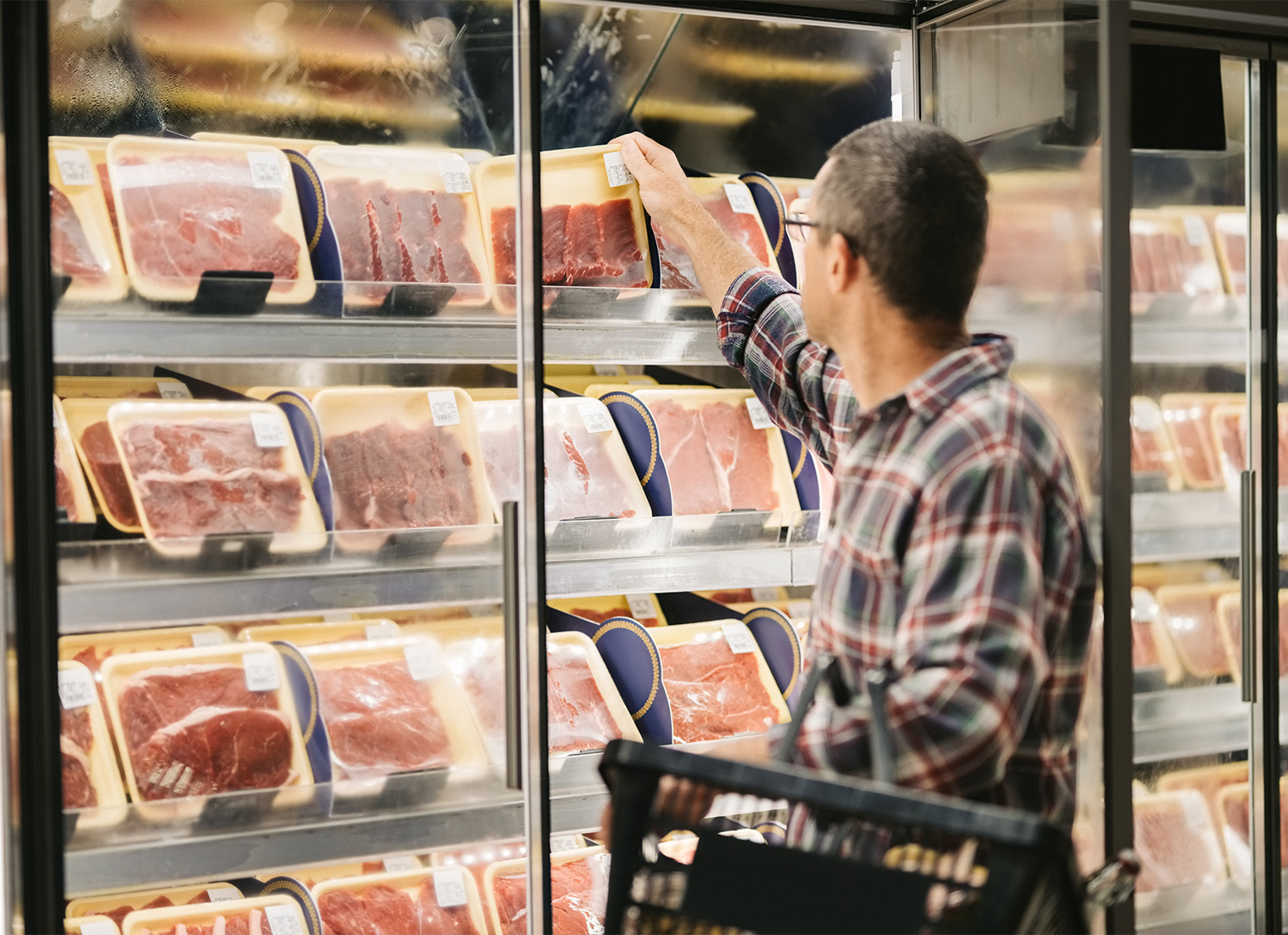 Male customer with a shopping basket taking meat from a fridge at local supermarket