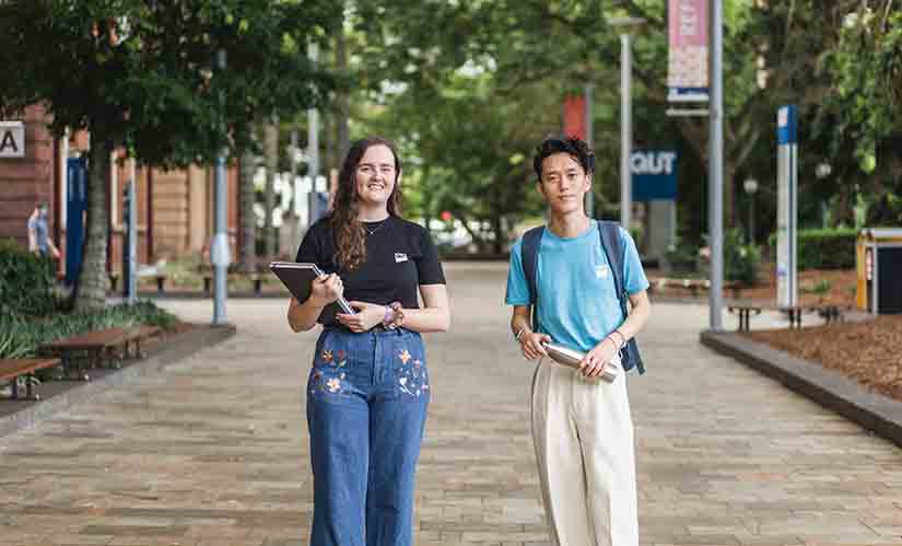 Two students carrying books walk together on campus.