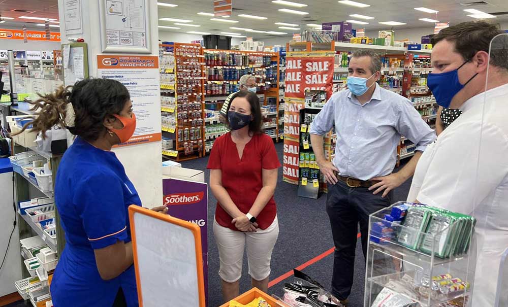 Female student in a pharmacy talks to customers while a qualified pharmacist supervises.
